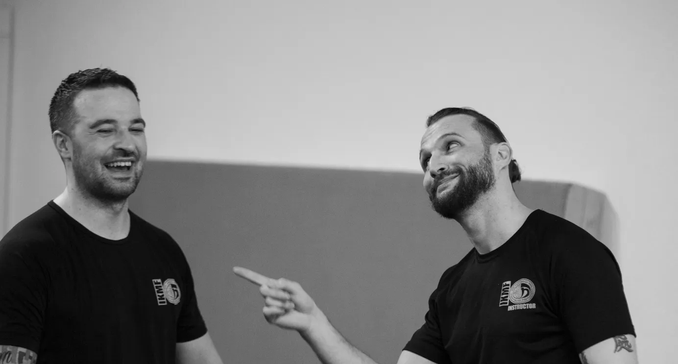 Zwei lachende Instruktoren in IKMF-Shirts im Trainingsraum